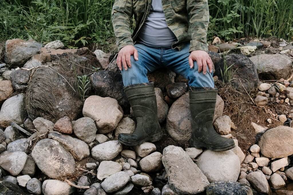 man sitting on rock, wearing rubber boots