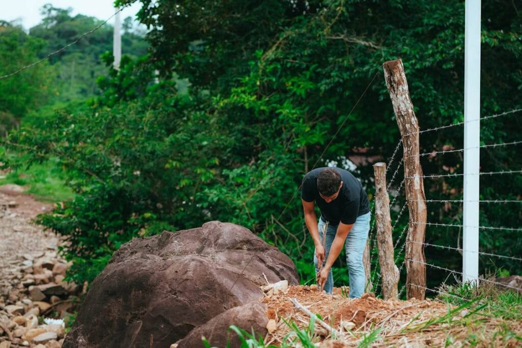 man digging hole near fence line