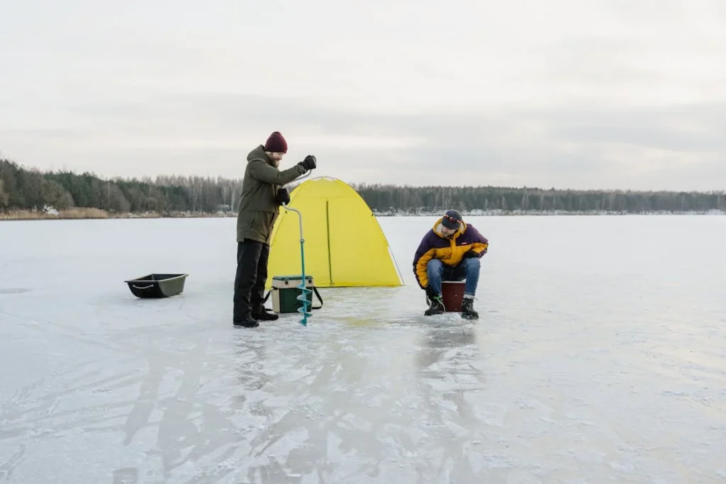 two men getting set up for ice fishing, one using hand auger